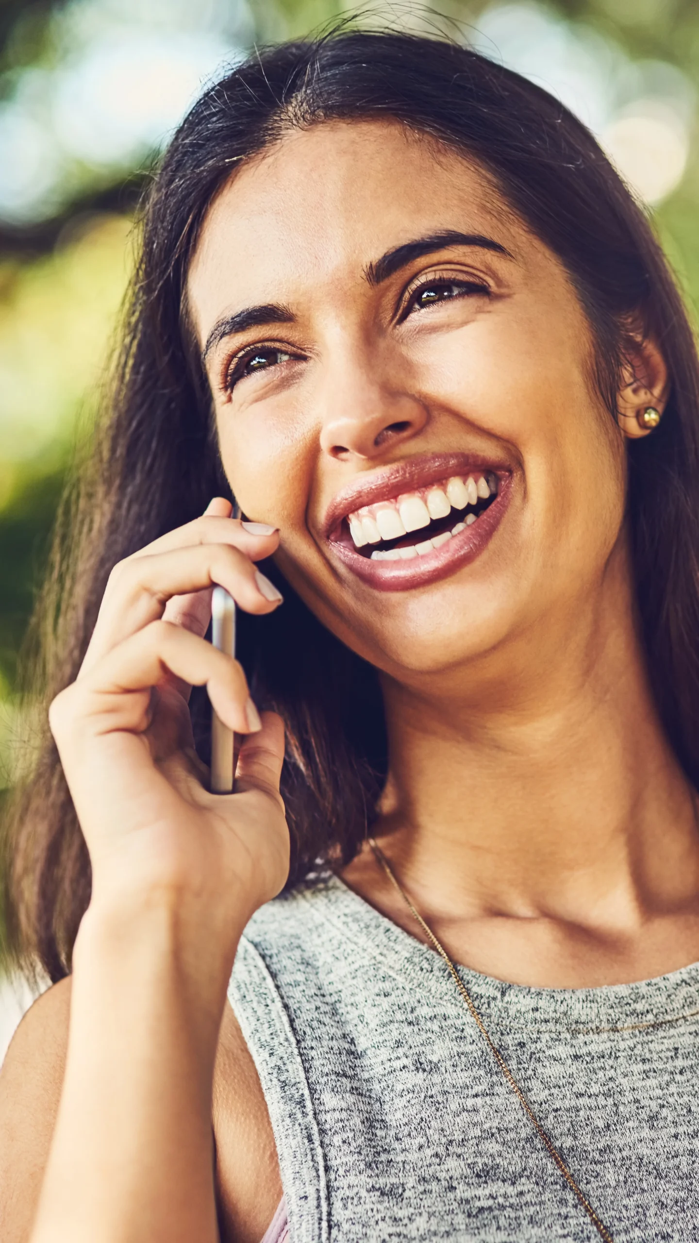Smiling woman talking on a smartphone outdoors with blurred greenery in the background